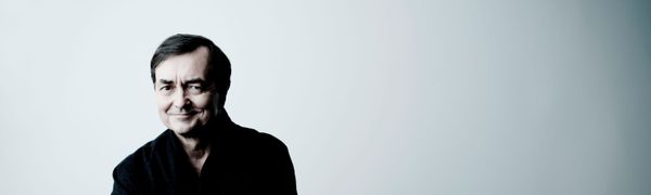 A man dressed in black sits in front of a white wall smiling at the camera