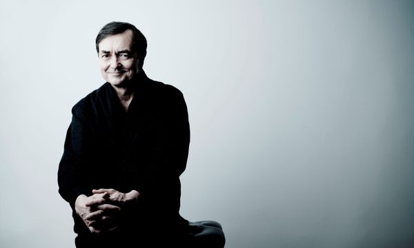 A man dressed in black sits in front of a white wall smiling at the camera