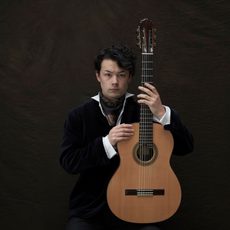 A man holding a guitar upright while looking into the camera