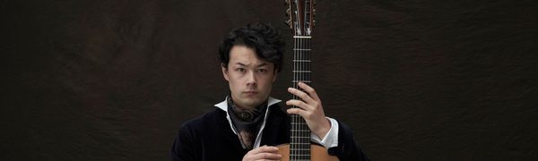 A man holding a guitar upright while looking into the camera