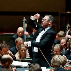 A conductor stands in front of an orchestra, conducting their performance