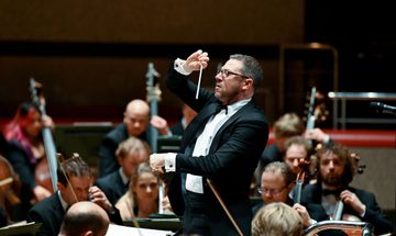 A conductor stands in front of an orchestra, conducting their performance