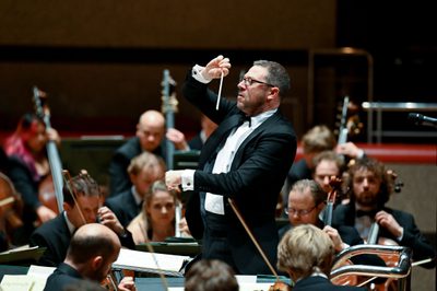 A conductor stands in front of an orchestra, conducting their performance