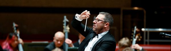 A conductor stands in front of an orchestra, conducting their performance
