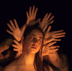 A woman's face surrounded by outstretched hands in a warm glow