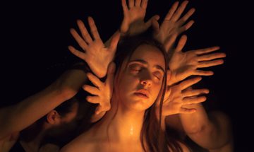 A woman's face surrounded by outstretched hands in a warm glow