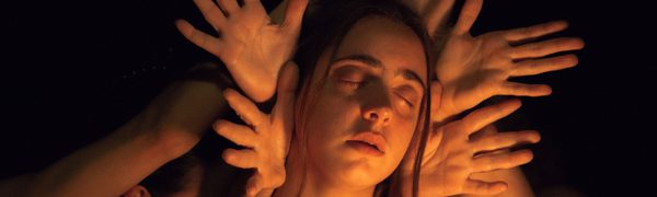A woman's face surrounded by outstretched hands in a warm glow