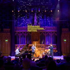 A group of jazz musicians perform on stage surrounded by an audience