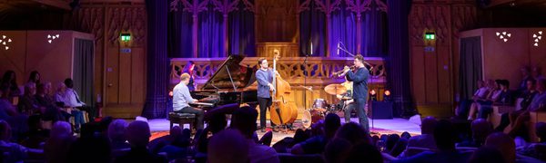 A group of jazz musicians perform on stage surrounded by an audience