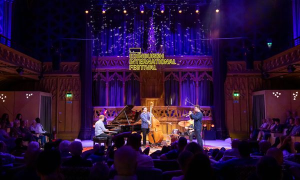A group of jazz musicians perform on stage surrounded by an audience