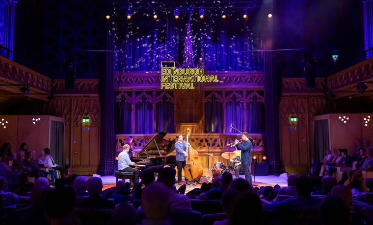 A group of jazz musicians perform on stage surrounded by an audience