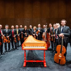 The Venice Baroque orchestra holding their instruments while standing around a keyboard instrument