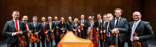 The Venice Baroque orchestra holding their instruments while standing around a keyboard instrument
