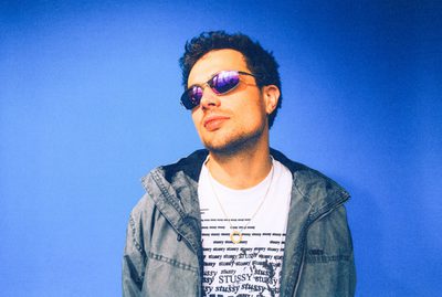 A man wearing sunglasses standing in front of a bright blue background