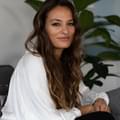 Nicola Benedetti sits on a sofa in a white shirt with long curly brown hair looking at the camera