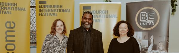 Three people stand in front of banners with Edinburgh International Festival and BE United branding on them