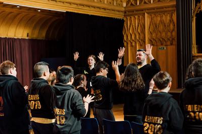 Group of children in black hoodies looking at two adults with their hands up during a workshop