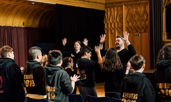 Group of children in black hoodies looking at two adults with their hands up during a workshop