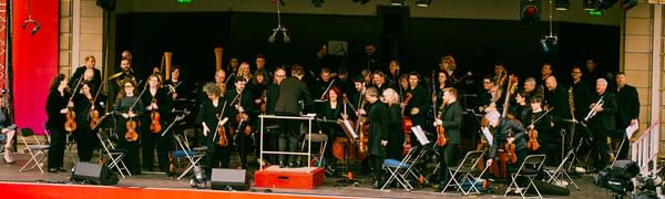 Orchestra on outside stage with red Virgin Money branding around the stage