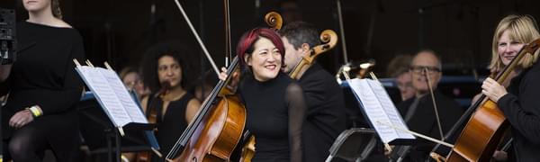 Orchestra on an outside stage, with musicians smiling