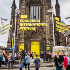 The Hub building with yellow doors and branding that reads 'Edinburgh International Festival'. People of all generations come and go