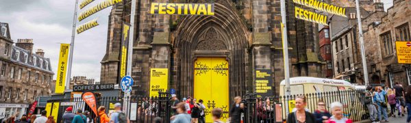 The Hub building with yellow doors and branding that reads 'Edinburgh International Festival'. People of all generations come and go