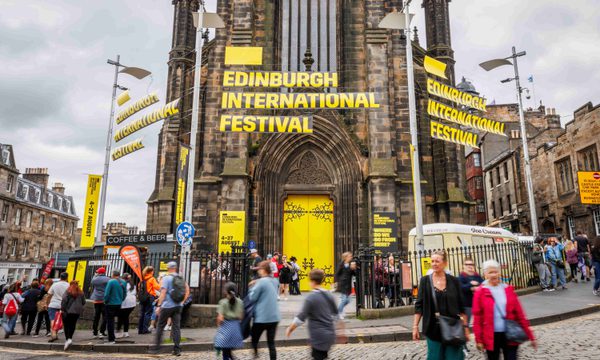The Hub building with yellow doors and branding that reads 'Edinburgh International Festival'. People of all generations come and go