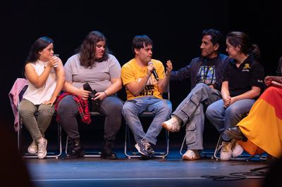 five actors sit on stage talking and smiling together