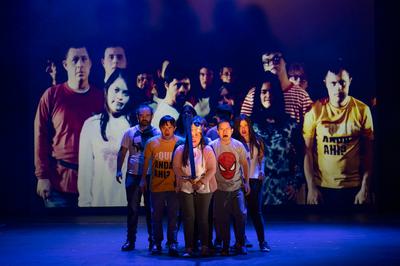 a group of actors stand together on stage in a triangle formation. The lady at the front holds a sword