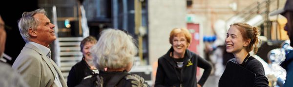 Edinburgh International Festival staff and audience members stand backstage chatting and laughing