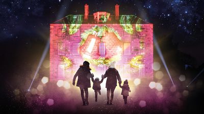 A family of four with two adults and two small children are silhouetted against a lit up house. The sky is starry above them.
