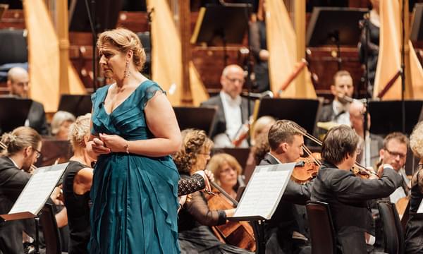 Woman in a blue dress stands in front of an orchestra