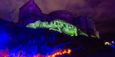 A huge green dragon is lit up through projections onto the side of a dark castle