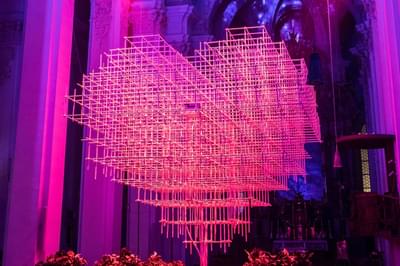 A huge pink 3D loveheart is made out of sticks and hangs from the ceiling of a church