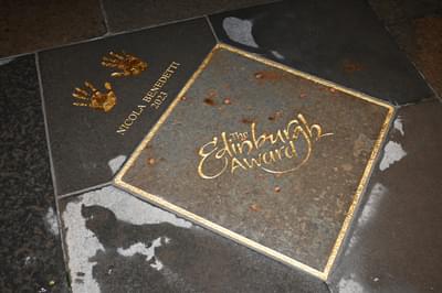 On the pavement there is gold-lined square with the gold lettering inside reading ‘The Edinburgh Award’. To the left of the square, there are gold handprints with the words ‘Nicola Benedetti 2023’ written.