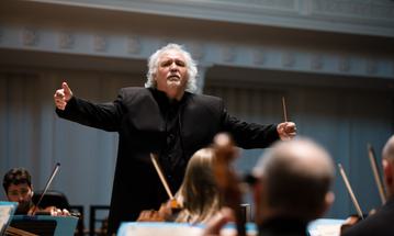 A man is standing in front of an orchestra, conducting