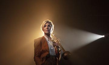 Woman standing holding wind instrument looking off camera, side lit by spotlight