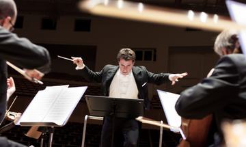 Man conducting orchestra with arms outstretched, looking down