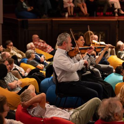 A group of people sitting on beanbags surround people playing the violin