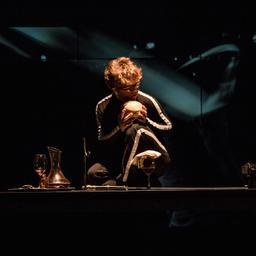 Man crouched on stage holding skull