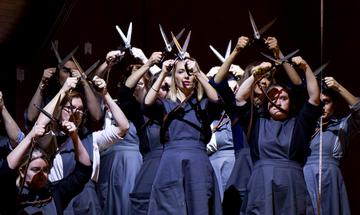 Group of women wearing blue dresses, holding scissors in the air above their heads