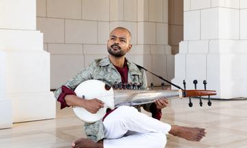 Man sitting cross legged on floor playing a stringed instrument