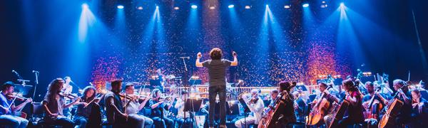 Orchestra performing on stage, conductor standing hands raised centre stage