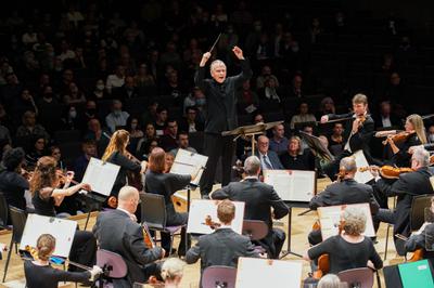 Man standing elevated centre stage conducting orchestra