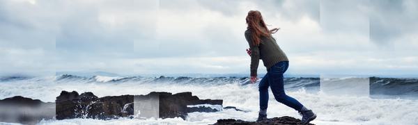Woman standing on a rocks in ocean facing out to sea