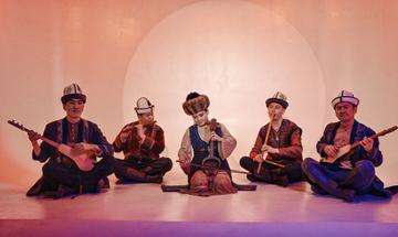 Five people seated on floor playing string and wind instruments