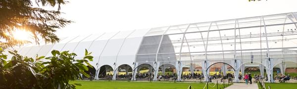 A large clear tent sits in the middle of a grassy plain.