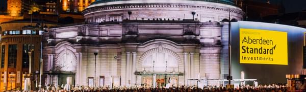 An illuminated Usher Hall with a crowd of people in front of him.