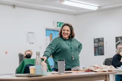 A woman wearing green stands smiling in a rehearsal room.