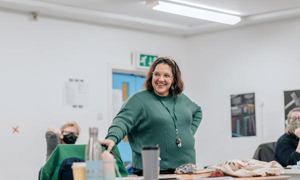 A woman wearing green stands smiling in a rehearsal room.